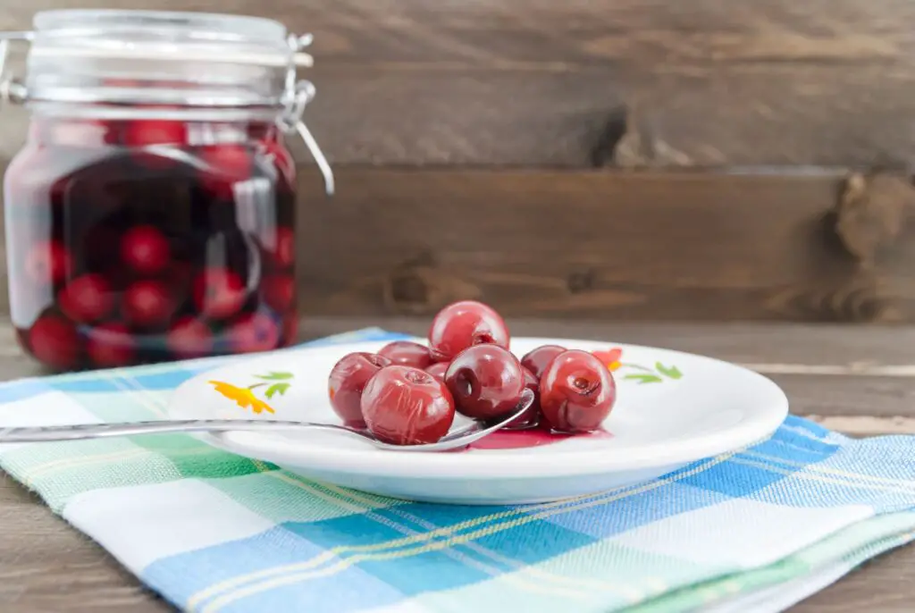 Sour cherries on white plate and in the background the jar with sour cherry compote